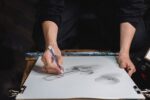 Person tecknar en skuggad figur med grafit på stort ritpapper